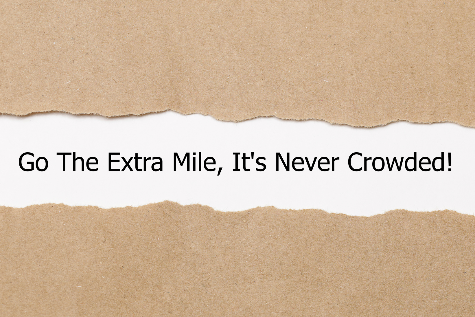 Motivational quote Go The Extra Mile It's Never Crowded appearing behind ripped paper.